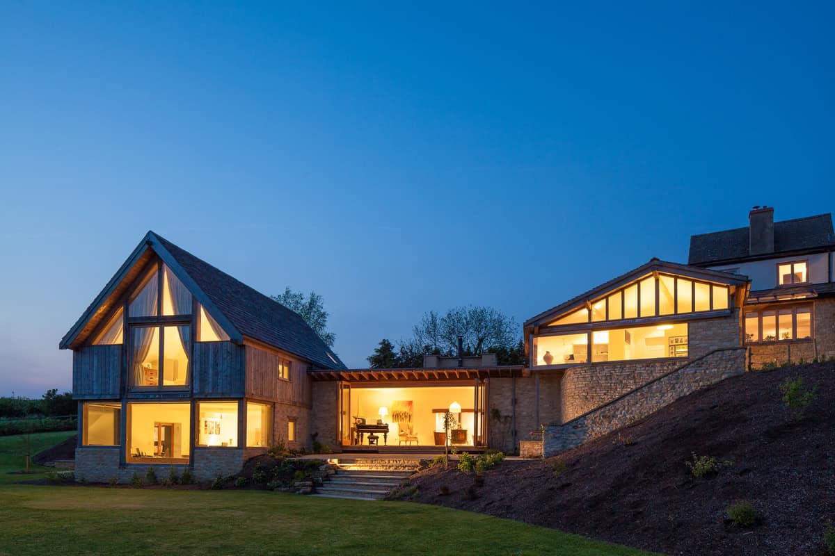 Cockadilly extension at dusk with illuminated timber-framed gable, stone walls and piano room