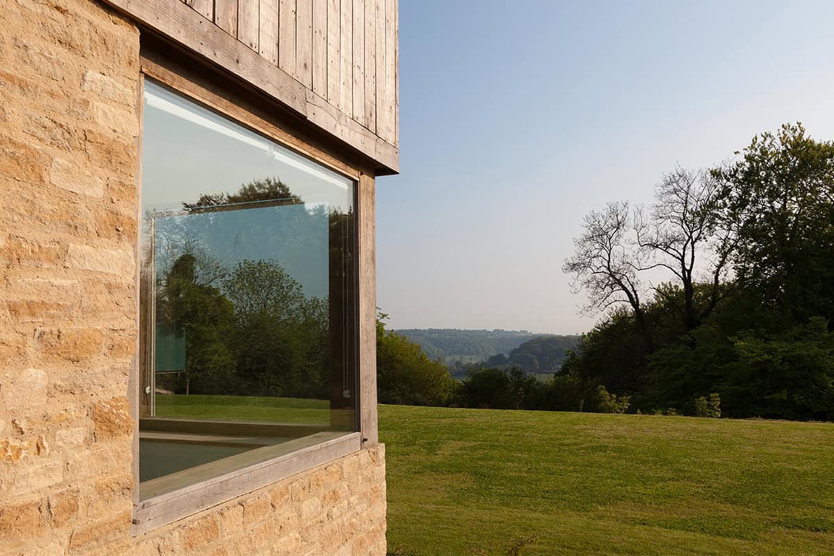 Cockadilly large glazed window in Cotswold stone wall framing valley views across green fields