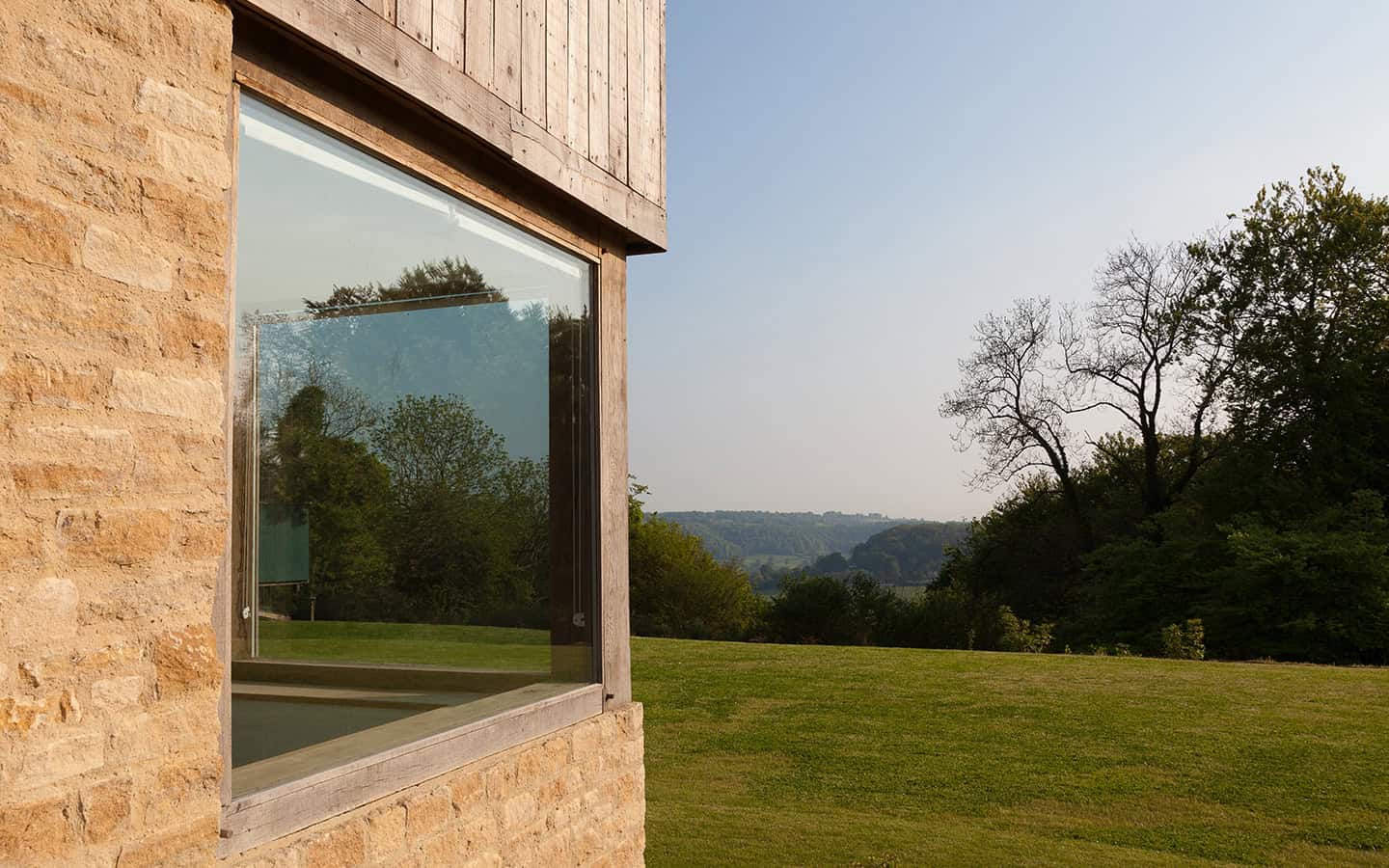 Cockadilly Cotswold stone wall detail with large picture window framing rolling countryside views