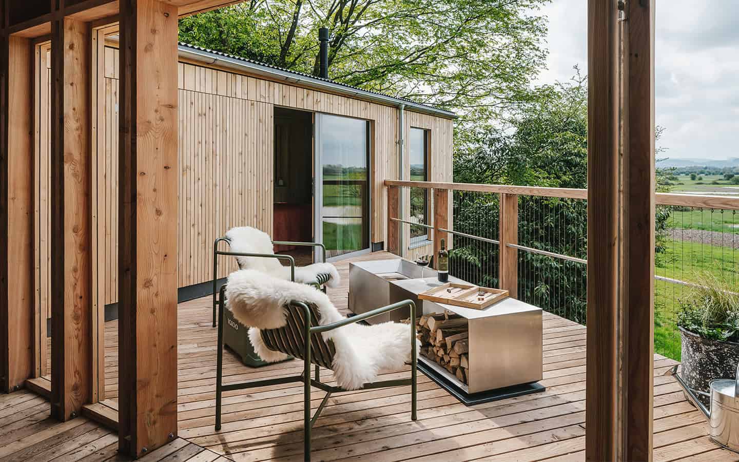 Elmore Treehouses timber-clad deck with sheepskin-draped chairs overlooking Gloucestershire countryside