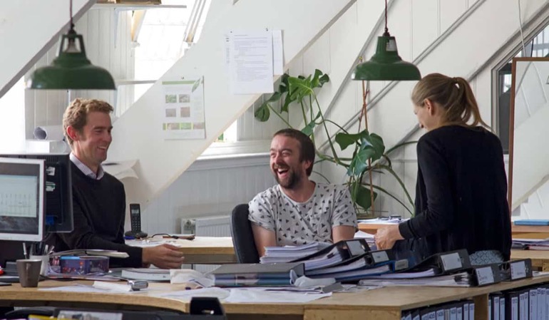 MHW team laughing together at their studio desks in St Mary's Mill, Chalford